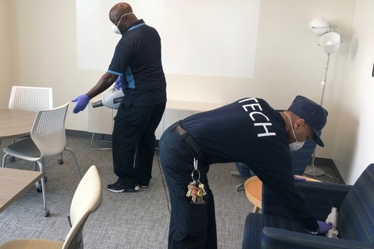 Wearing appropriate PPE, event management technician Lester Hardy (on left) and event management lead Darryl Flemming sanitize a meeting room in the ESC. 